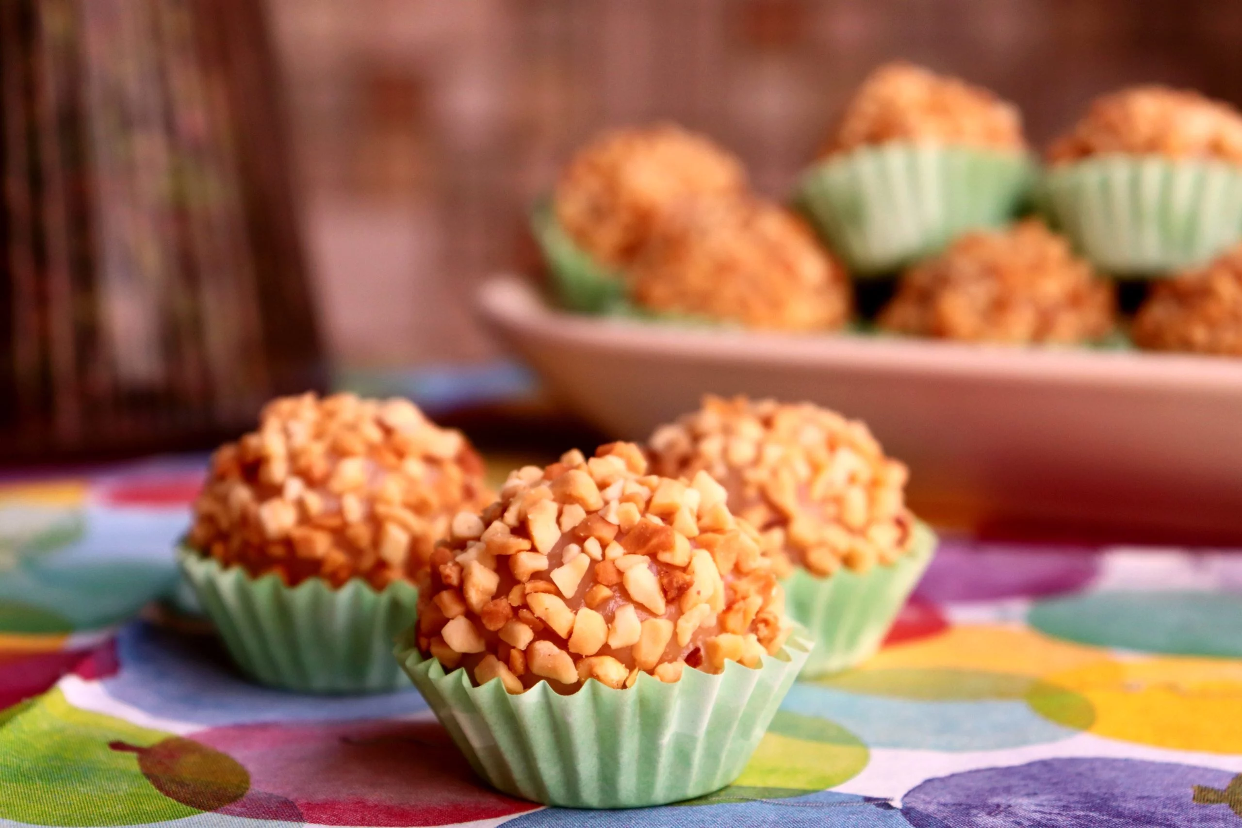 imagem mostra tres amendoim e ao fundo um prato com mais brigadeiros
